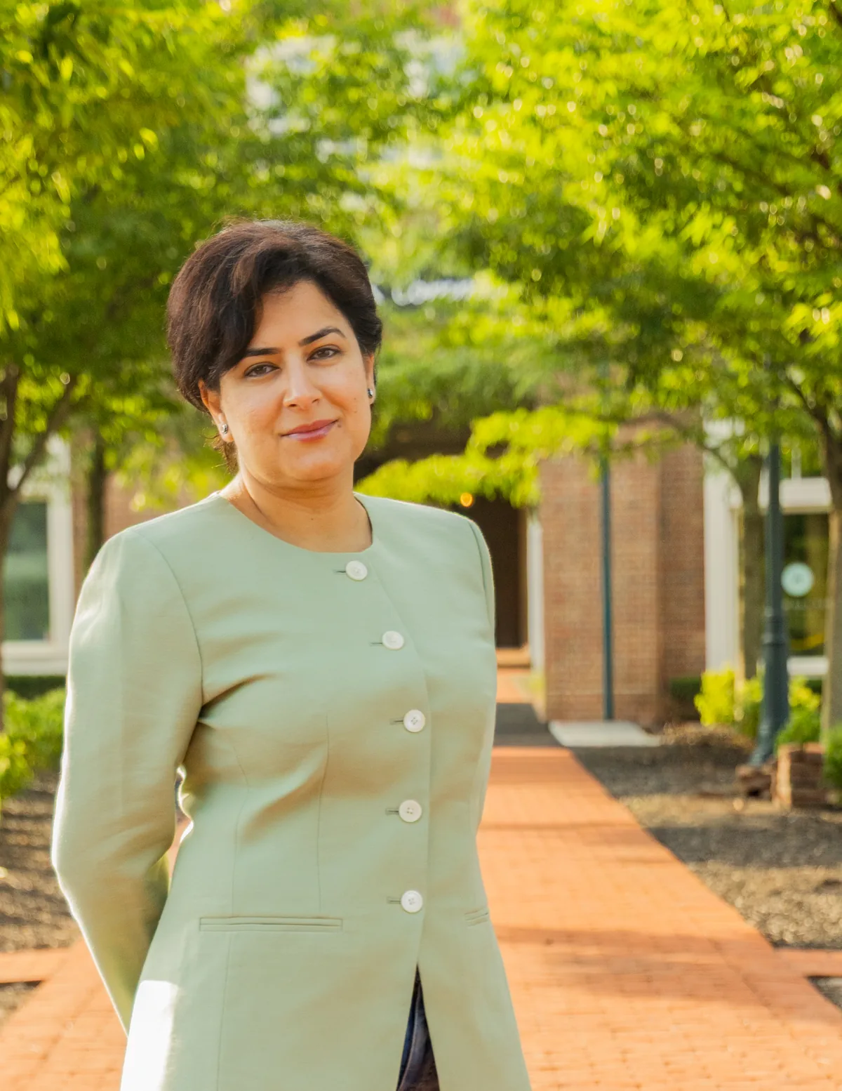 Dr. Mira Massoud, founder of Imperfect Medical, standing on a tree-lined brick path